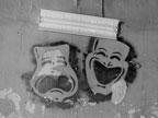 Comedy and tragedy masks spray-painted onto a ceiling, with a florescent light set above them.